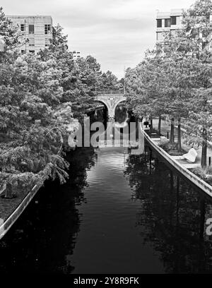 Wasserstraße mit Gehwegsbrücke und Gebäuden in The Woodlands TX in Schwarz und weiß Stockfoto