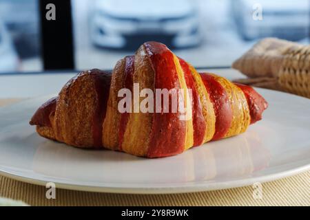 Das goldbraune Croissant sitzt einladend auf einem Teller neben einer strukturierten Leinenserviette in gemütlicher Atmosphäre Stockfoto