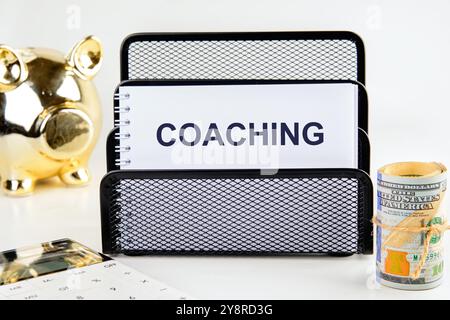 Geschäftskonzept. Der Satz, Text, Wortwahl COACHING wird auf einem weißen Blatt in einem Ständer auf hellem Hintergrund geschrieben. Stockfoto