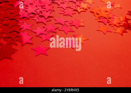Abstrakter Hintergrund mit rotem Konfetti in Form eines Sterns auf rotem Hintergrund mit Kopierraum. Konfetti in Form von roten Sternen als Hintergrundstruktur. Stockfoto