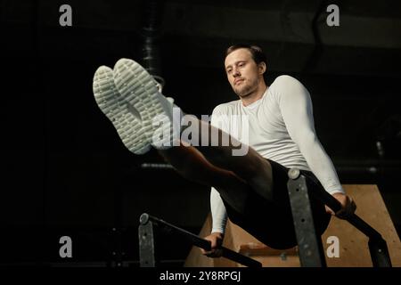 Schuss aus niedrigem Winkel eines starken Mannes, der den L-Sitz perfekt durchführt, während er Stabilitätsübungen im Fitnessstudio trainiert Stockfoto