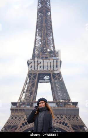 Pariser Frau in Beret und grauem Mantel posiert auf dem Highway mit Eiffelturm Stockfoto