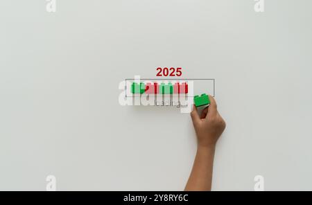 Laden von Neujahr 2024 bis 2025 mit Kinderhand, die grünen Kunststoffblock in Progress-Leiste steckt. Starten Sie das neue Jahr 2025 mit Zielplan, Zielkonzept und Strategie. Stockfoto