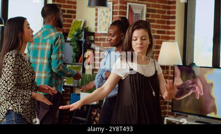 Multiethnische Frauen tanzen im Haus während einer unterhaltsamen Apartmentparty, eine Gruppe von Freunden genießt lebhafte Musik, tanzt und trinkt Wein bei einem geselligen Treffen. Stockfoto