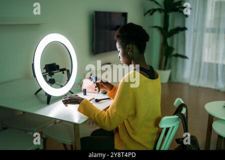 Eine Frau ist zu Hause und erstellt Inhalte mit einem Ringlicht und einer Kamera für ihr Online-Publikum Stockfoto