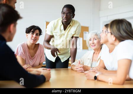 Freundliche afroamerikanische Englischlehrerin, die Sprachkurse für eine Gruppe von Erwachsenen gibt Stockfoto