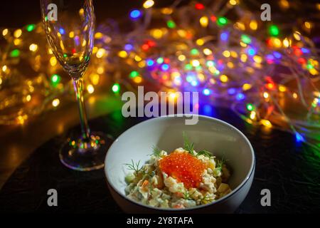 Schüssel olivier-Salat mit rotem Kaviar garniert mit Dill auf dem Tisch mit Sektflöte und Girlande auf dem Hintergrund Stockfoto