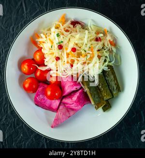 Teller mit Sauerkraut, Gurken und Gemüse auf dunklem Hintergrund Stockfoto