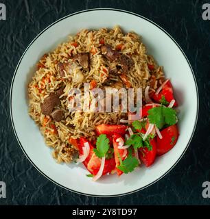 Traditionelles usbekisches Pilaw mit Lammfleisch und frischem Tomatensalat auf einem Teller Stockfoto
