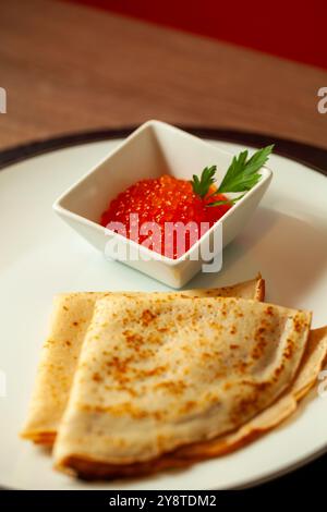 Traditionelle russische Pfannkuchen mit rotem Kaviar und Petersilie werden auf weißem Teller serviert Stockfoto