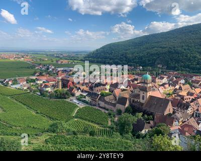 Aus der Vogelperspektive auf Kaysersberg, Elsass, Frankreich, mit Weinbergen und grünen Hügeln unter hellem Himmel. Das Dorf verfügt über traditionelle Häuser und ein historisches Stockfoto