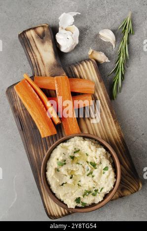 Flacher Laienblick auf die mit Kichererbsen und Olivenöl bestockte Gemüsesummus-Dip-Schüssel, serviert mit Karottscheiben Stockfoto