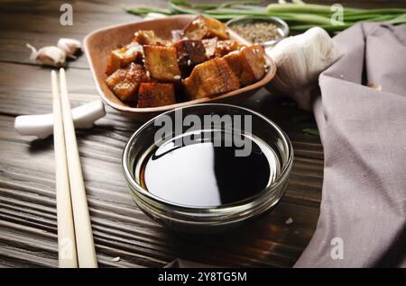 Knusprig rühren gebratenen Tofu-Würfel mit Schnittlauch in Tonschale auf Holzkochtisch mit Serviette Schnittlauch Pfeffer Knoblauch und Sojasoße beiseite Stockfoto