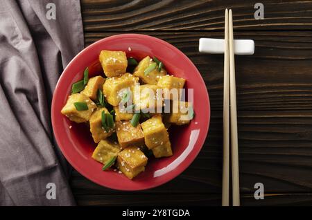 Flach legen Blick auf knusprig tief rühren gebratenen Tofu Würfel mit Schnittlauch in Tonschale auf hölzernen Küchentisch mit Serviette beiseite Stockfoto