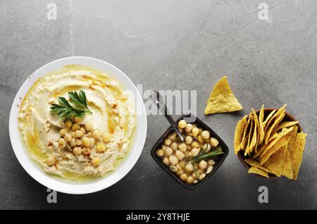 Flacher Lay Hummus in Tonform mit Kichererbsen und grünen Korianderblättern auf Steintisch serviert mit Tortilla-Chips Stockfoto