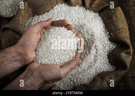 Menschliche Hände halten eine Hand voll Reis über einem Leinensack Stockfoto