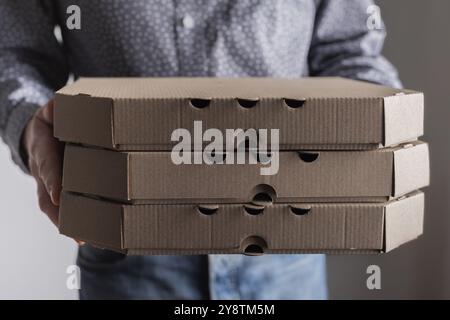 Kaukasische männliche Hände halten drei Pizzaschachteln in Vorderansicht mit Kopierraum Stockfoto