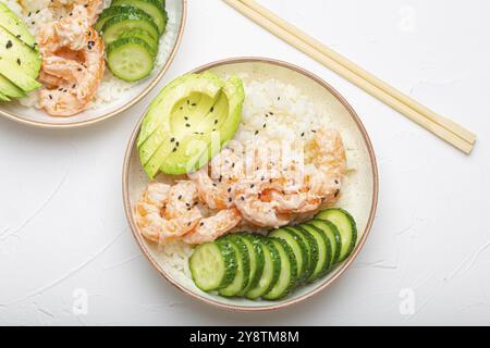 Zwei weiße Keramikschalen mit Reis, Garnelen, Avocado, Gemüse und Sesamsamen und Holzstöcken auf weißem Betonsteinhintergrund von oben. Gesundheit Stockfoto