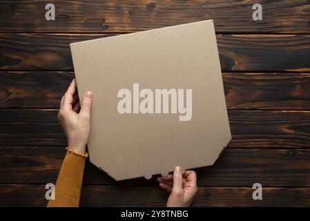 Pizza geschlossene Kartonbox in kaukasischen Händen auf natürlichem dunklem Holztisch flach aufgelegtes Modell mit Kopierraum Stockfoto