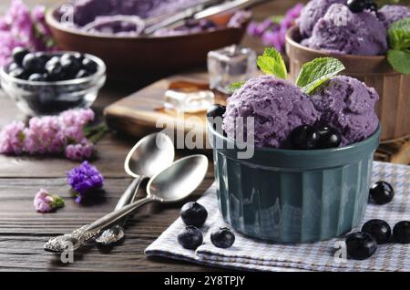 BlackBerry Eiscreme-Kugeln in Tonschüsseln auf einem hölzernen Küchentisch mit Blumen und Beeren zur Seite Stockfoto