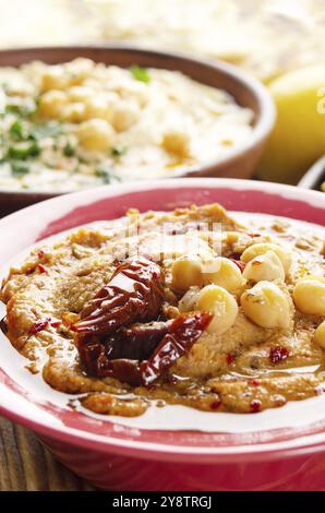 Frischer hausgemachter Hummus in Tonform mit Olivenöl, Kichererbsen, Gewürzen und sonnengetrockneten Tomaten auf Steintisch Stockfoto