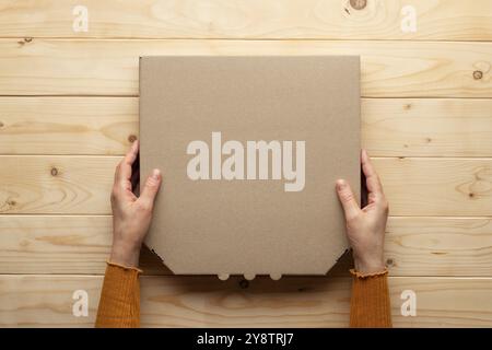 Pizza geschlossene Kartonbox in menschlichen kaukasischen Händen auf natürlichem Holztisch flach aufgelegtes Modell mit leerem Platz Stockfoto