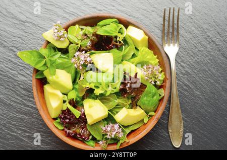 Draufsicht auf Lehm Gericht mit Salat mit Avocado, grün und violett Kopfsalat, Feldsalat und Oregano Blumen auf schiefer Fach mit Gabel beiseite Stockfoto