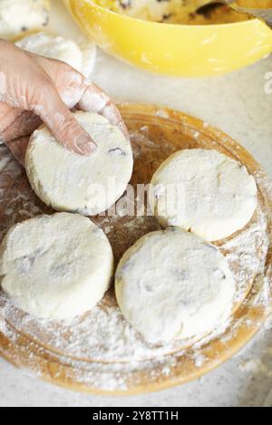 Kaukasische Frauenhände machen Hüttenkäse-Pfannkuchen mit Rosinen-Kochhintergrund Stockfoto