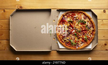 Peperoni-Pizza mit Paprika, Zuckermais und Rucola in offener Schachtel auf natürlichem Holzküchentisch, flacher Lay View mit Kopierraum Stockfoto