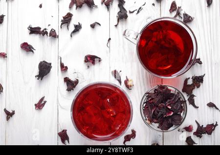 Draufsicht bei zwei Tassen mit Eis und trockenen Hibiscus Blüten auf Weiß Holztisch Hintergrund Stockfoto