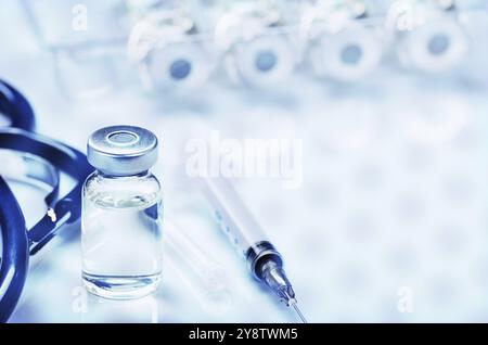 Fläschchen mit flüssigem Medikament als Impfdosis Grippeimpfung zusammen mit Stethoskop, Spritze für Injektionsbehandlung auf medizinischem Tisch. Impfung oder Immunisierung c Stockfoto