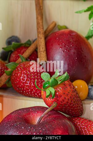 FRISCHE UND GESUNDE FRUCHTMISCHUNG, ERDBEEREN, ÄPFEL UND ZIMT IN EINER KREATIVEN ZUSAMMENSETZUNG, MIT HÖLZERNEM HINTERGRUND Stockfoto