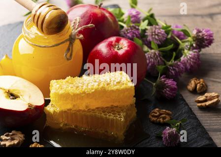 Einmachglas mit Honig, Honigtaube, Honigwabe, roten Äpfeln und Walnüssen auf Küchentisch Stockfoto