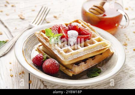 Belgische Waffeln serviert mit Erdbeeren und Minzblatt bestäubt Puderzucker auf weißem Holzküchentisch mit Sirup zur Seite Stockfoto