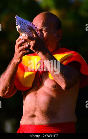 Ein Mann in traditioneller hawaiianischer Kleidung bläst durch eine Muschelmuschel und begrüßt Gäste am Waikiki Beach, Hawaii Stockfoto