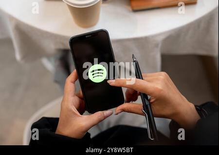 Chiang Mai, Thailand - 03. Oktober 2024: Eine Nahaufnahme einer Frau, die ein iPhone mit dem Spotify-Logo auf dem Bildschirm hält. Eine Frau, die die Spotify-Anwendung verwendet Stockfoto