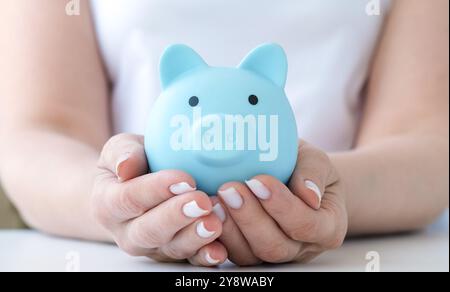 Weibliche Hände, die blaue Schweinebank halten. Geld sparen und schützen, Ruhestand und Budget Stockfoto