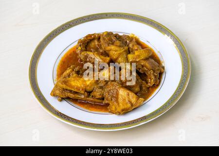 Köstliches hausgemachtes Hühnercurry oder Hühnchen-Bhuna auf einem weißen Teller, auf hellem Holz. Stockfoto