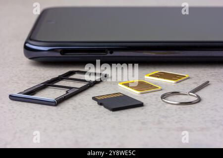 Smartphone mit offenen Steckplätzen für Micro SD- und Nano-SIM-Karten, zwei Nano-SIM-Karten und Metallschlüssel auf grauem Hintergrund Stockfoto