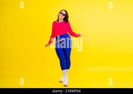 Hübsch lächelnde, pralle Frau in einem sportlichen Oberteil und Leggings, die ein Springseil in den Händen hält Stockfoto