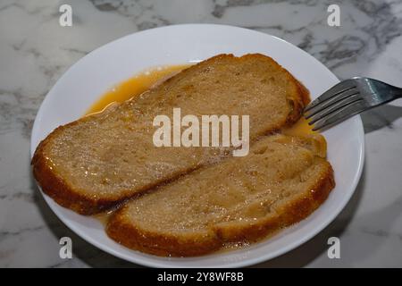 Ein Teller mit zwei Stücken Eierteigbrot mit einer Gabel drauf. Der Teller ist weiß und der Toast ist mit Ei bedeckt. Stockfoto