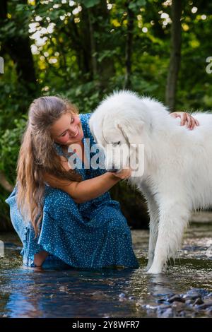 Die junge Frau und ihr großer weißer Hund der Großen Pyrenäen genießen die gemeinsame Zeit und kühlen sich an heißen Sommertagen in einem Fluss ab. Haustierbesitzer, Haustierliebhaber, Hund fr Stockfoto