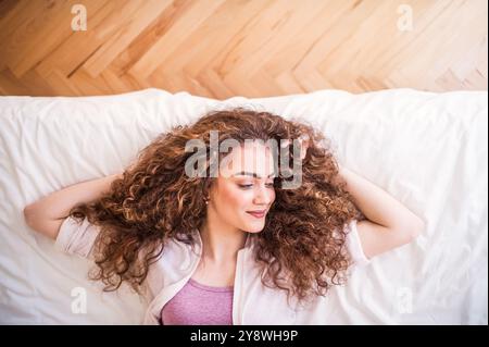 Porträt einer schönen jungen Frau mit einem lockigen Haar, das auf dem Rücken auf dem Bett liegt. Draufsicht. Stockfoto