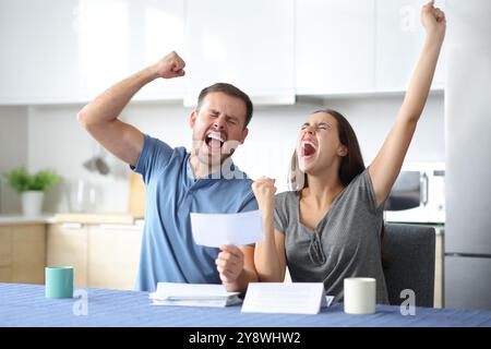 Ein aufgeregtes Paar, das gute Nachrichten feiert und in der Küche zuhause Quittung hält Stockfoto