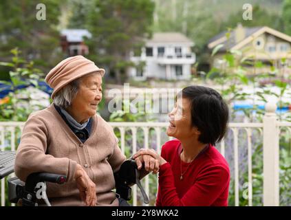 Eine ältere Frau sitzt auf dem Gehhilfen. Eine schöne Zeit mit ihrer Tochter zu Hause im Garten. Stockfoto