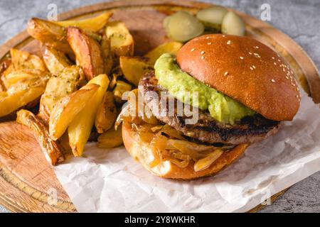 Burger mit karamelisierter Zwiebelsauce und Avocado auf einem Holzschneidebrett Stockfoto