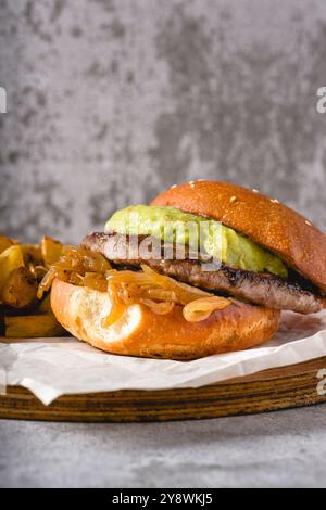 Burger mit karamelisierter Zwiebelsauce und Avocado auf einem Holzschneidebrett Stockfoto