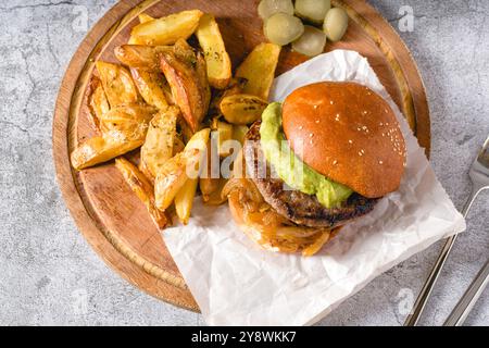 Burger mit karamelisierter Zwiebelsauce und Avocado auf einem Holzschneidebrett Stockfoto