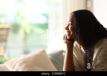 Seitliches Porträt einer glücklichen schwarzen Frau, die durch ein Fenster in einem Haus schaut Stockfoto