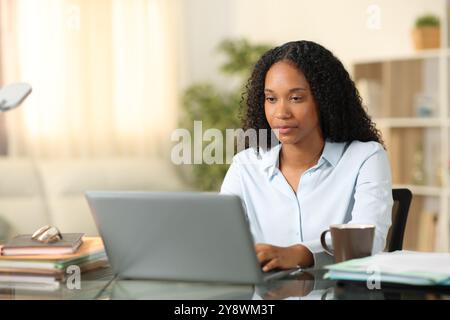 Seriöse schwarze Geschäftsfrau, die zu Hause online mit einem Laptop arbeitet Stockfoto